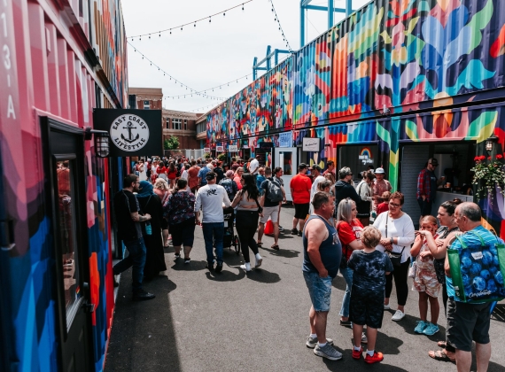 People walking along a colourful outdoor market at a festival.