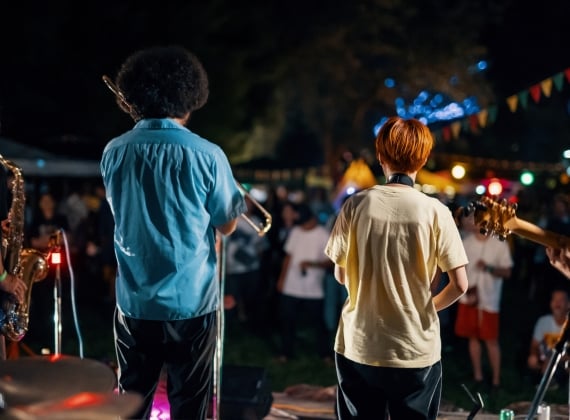 Musicians playing saxophone, trombone and guitar from behind looking from the stage onto the crowd.