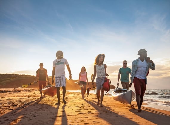 Surfers carry kayaks across the beach