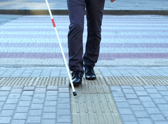 A person using a White mobility cane to traverse a street