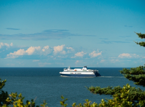 A large ferry sailing in the ocean from a distance on a sunny day, blue skies with a few clouds.