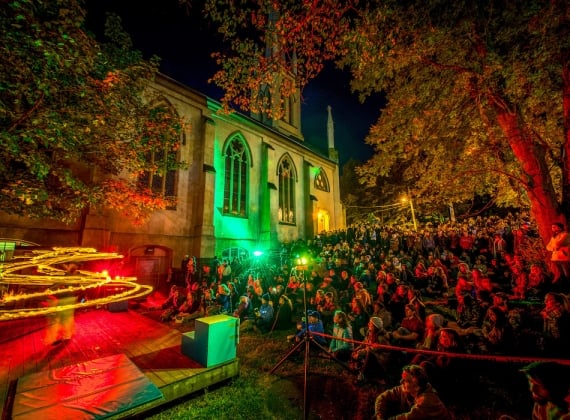 A group of spectators watch a colourful performance at night on church grounds.