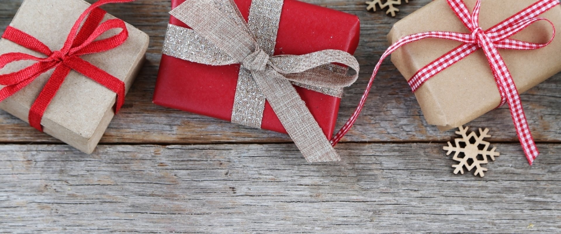 3 gifts wrapped in red and brown wrapping paper on a wooden back drop with fir branches and snowflake decorations.