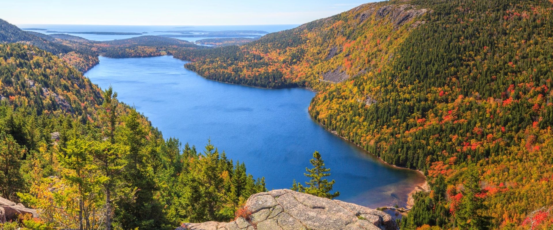 Looking down at a large pond in a lush green and red valley from a cliff on a sunny day.