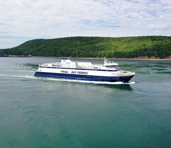 A ferry sailing in calm waters with lush green hills in the background.